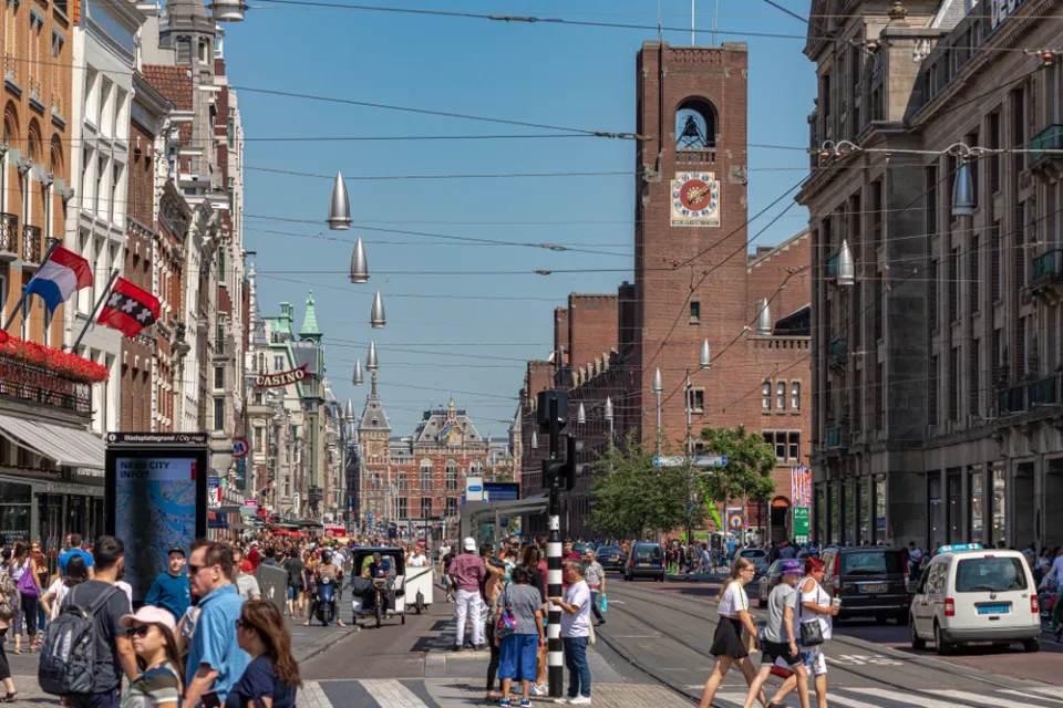 Crowded Amsterdam street with pedestrians, cars, and church in background